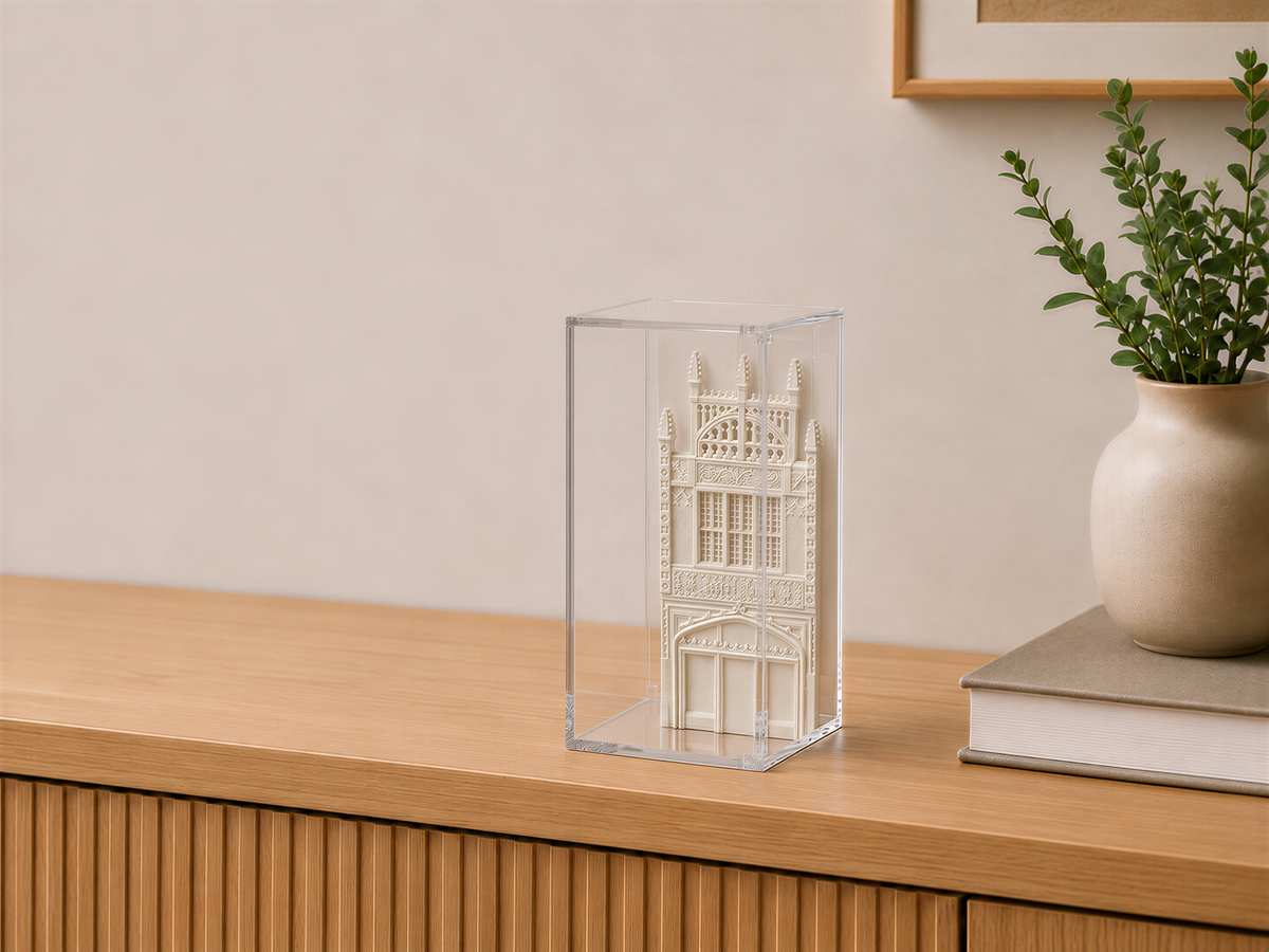 a wooden cabinet with a clear glass display case containing a miniature model of a building, placed on a wooden surface next to a plant in a vase.