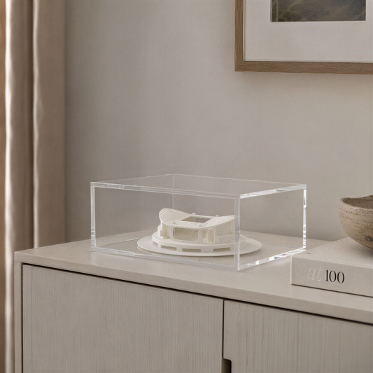 a clear glass display case containing a white model of a building, placed on a white cabinet or shelf.