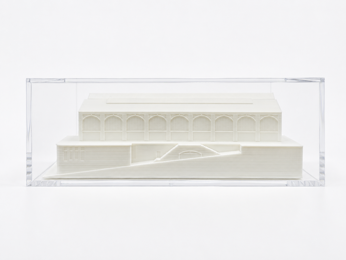 A white 3D model of a building, displayed in a clear plastic case.